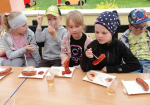 dzieci jedzą kiełbaski z grilla